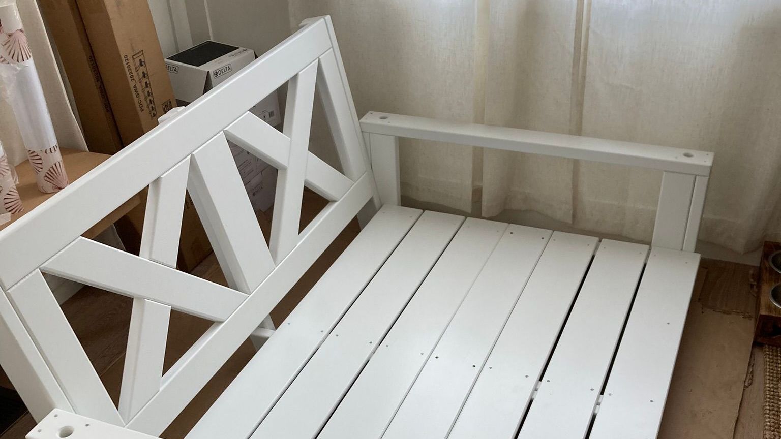 A white wooden bench is sitting in front of a window.