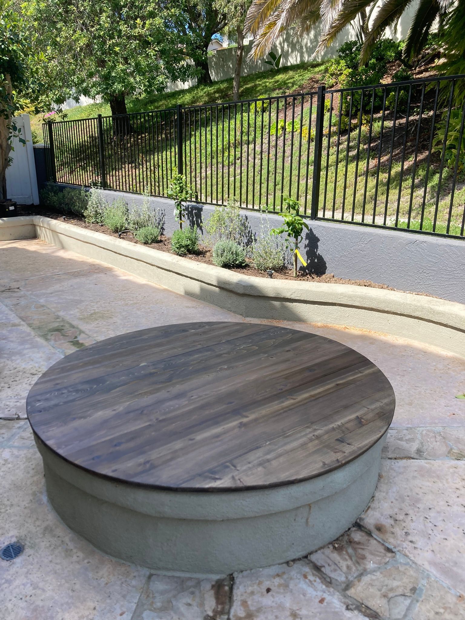 A wooden table with a wooden top is sitting on a patio next to a fence.
