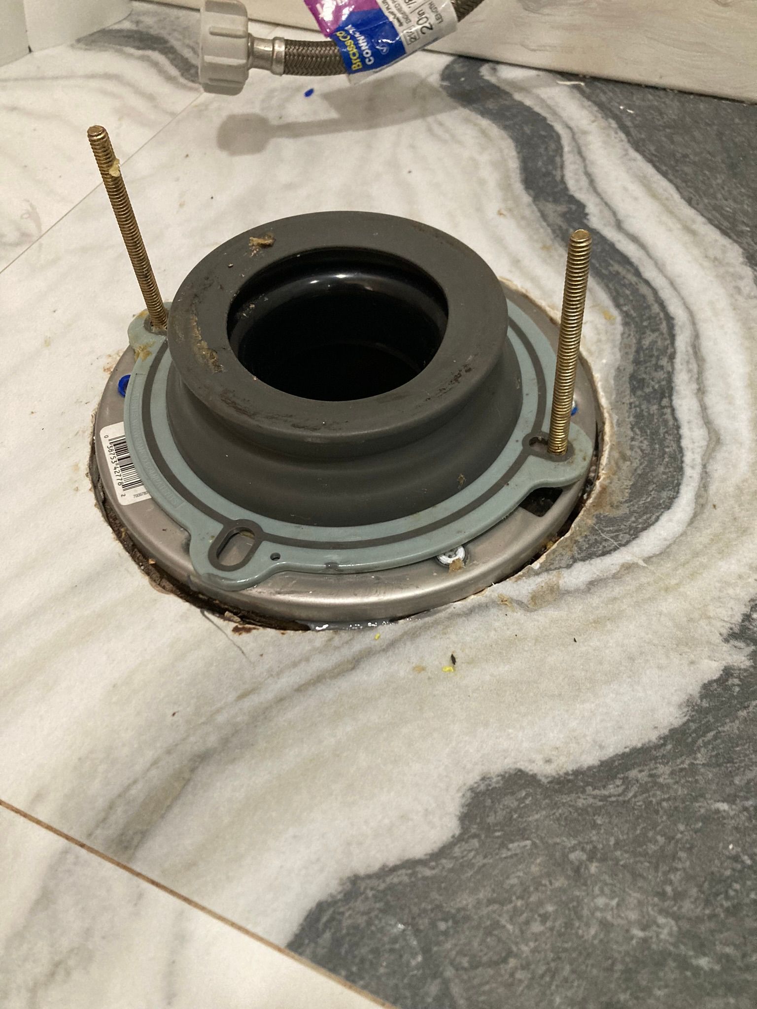 Toilet flange installed on marble tile floor, with mounting bolts in place.