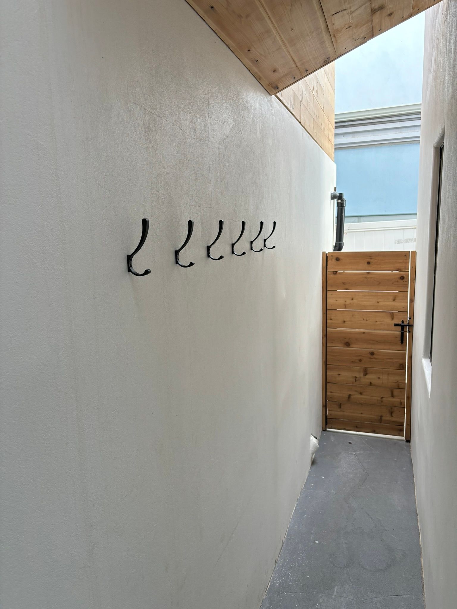 A white wall with hooks on it and a wooden gate.