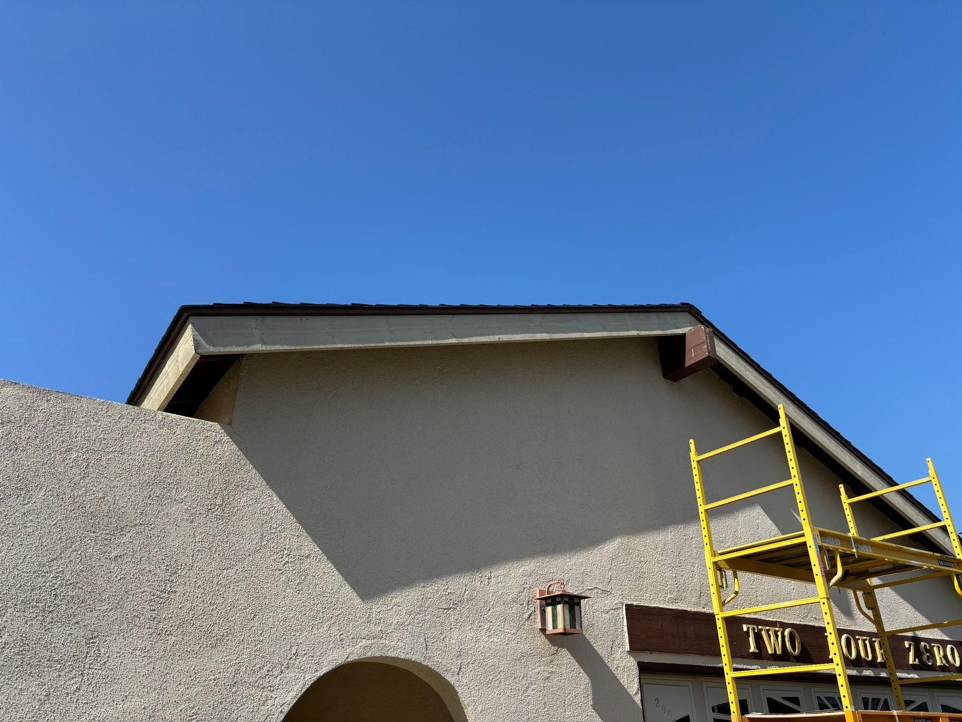 Beige building with dark roof against a blue sky, scaffolding at the right.