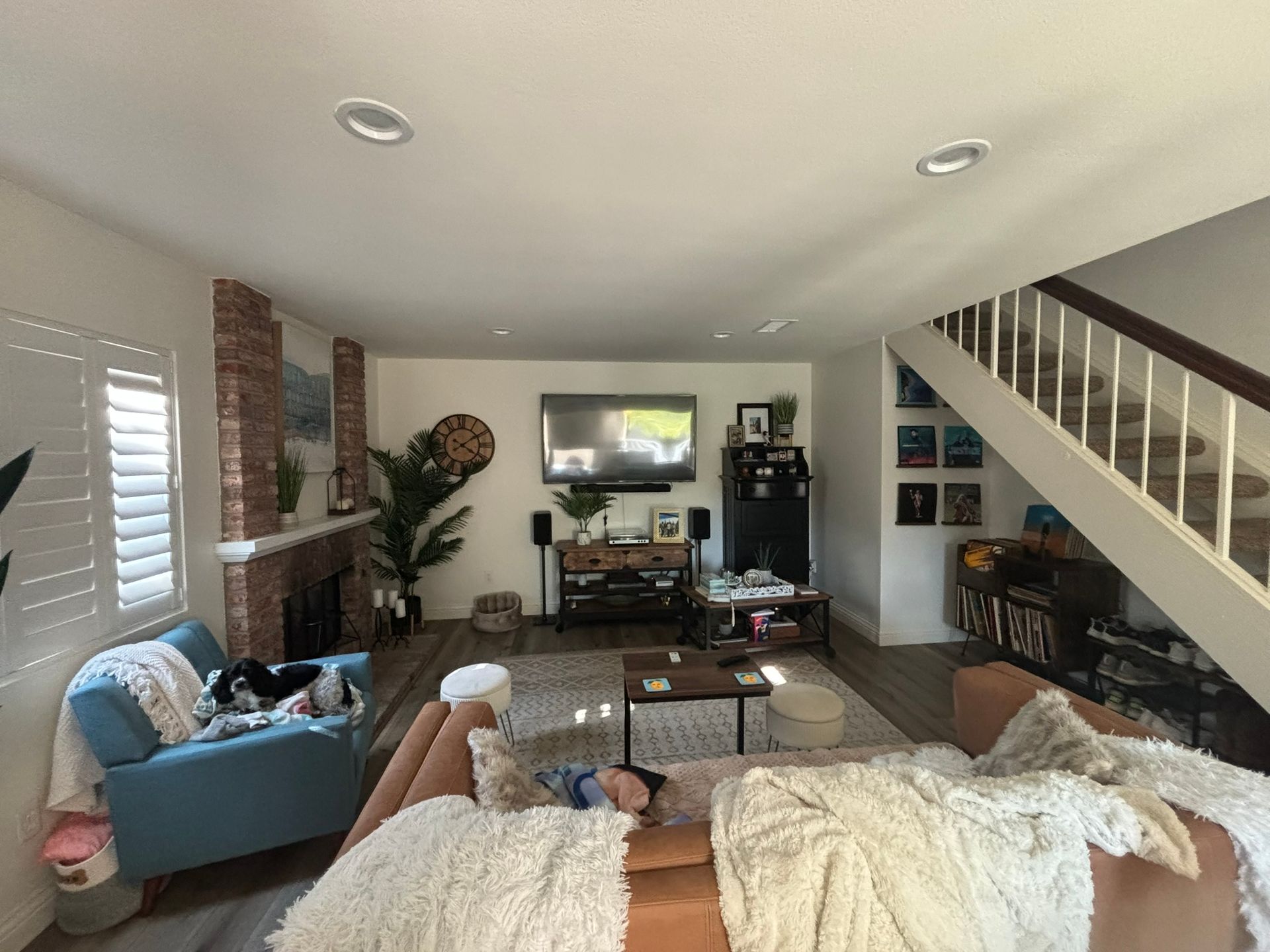 A living room with a couch , chair , television , fireplace and stairs.