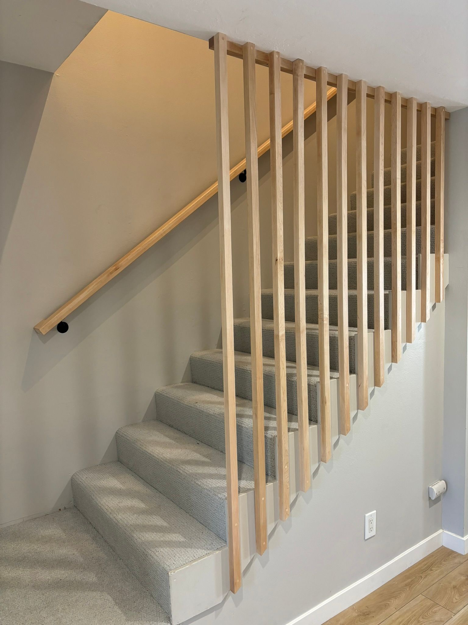 Staircase with carpeted steps, a light wood handrail, and vertical wood slats for the railing.
