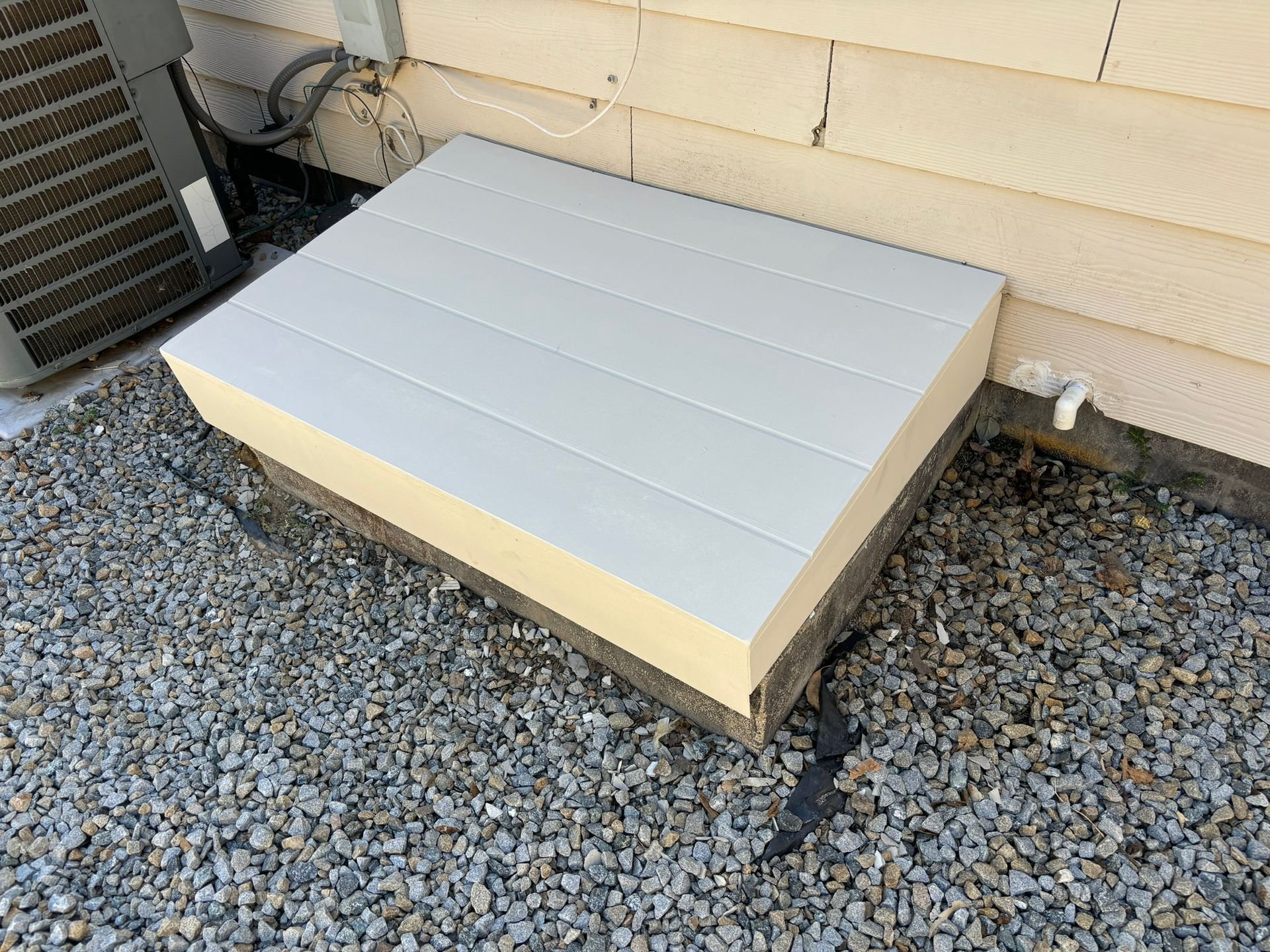 A white box is sitting on top of a pile of gravel next to a house.
