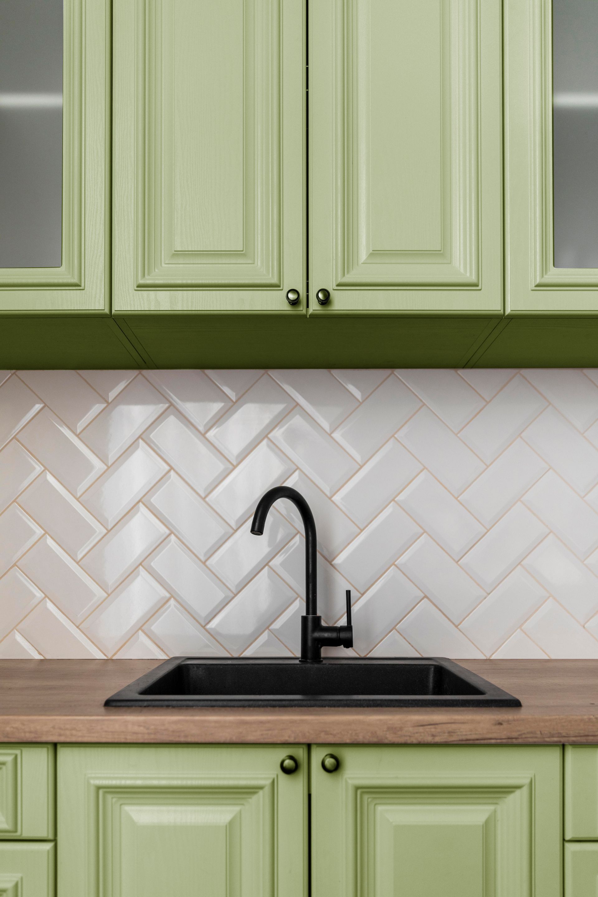 A kitchen with green cabinets and a black sink.