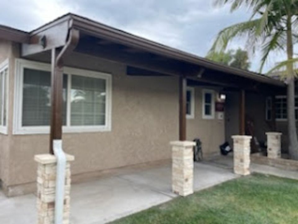 Brown awning over a tan stucco house with light-colored stone columns and green grass.