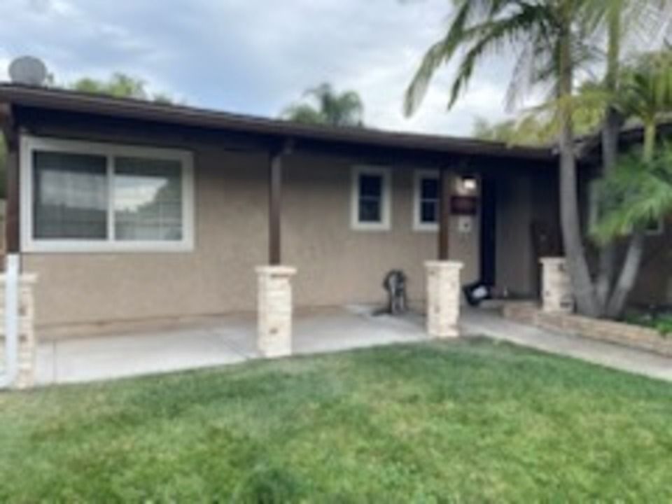 Tan single-story house with columns, a porch, and a grassy lawn in front. Palm trees are visible.