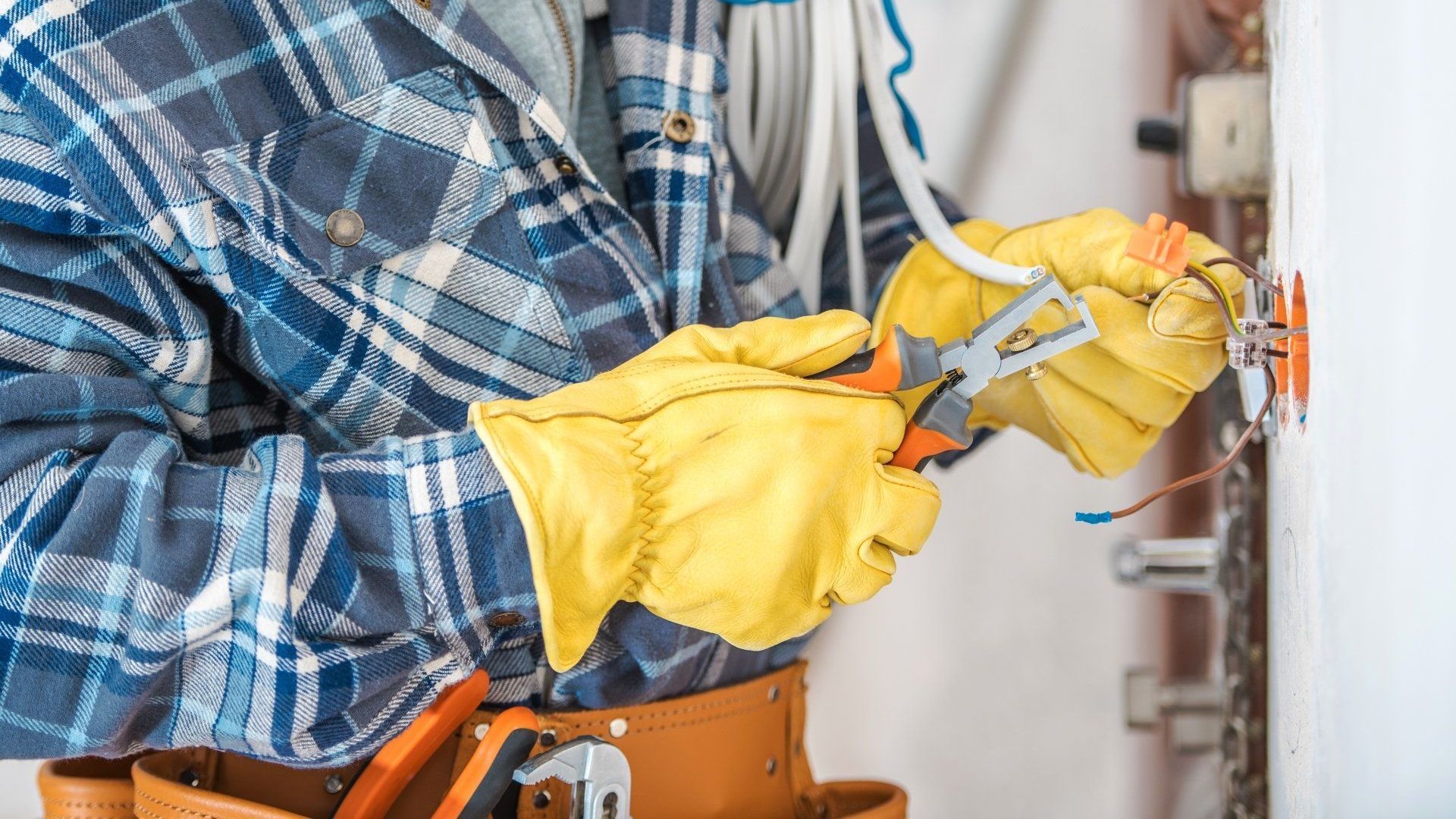 An electrician is working on an electrical outlet on a wall.