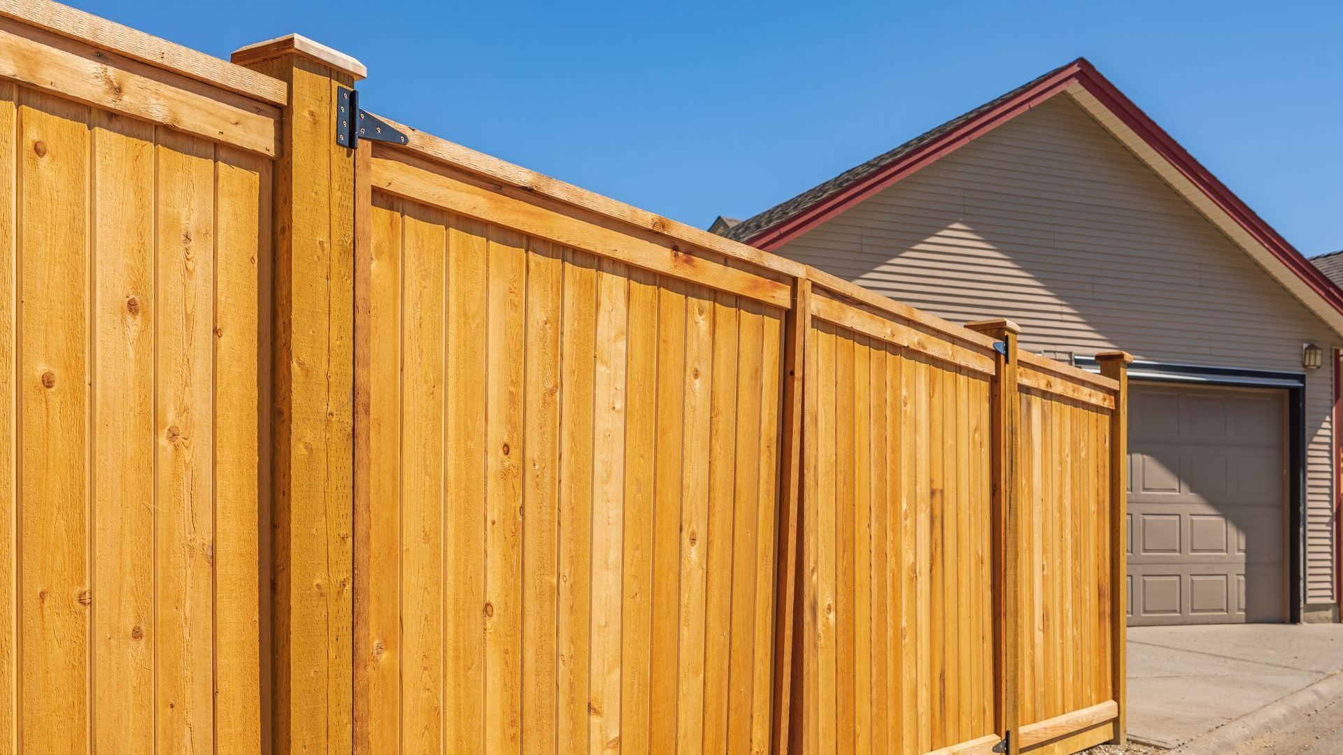 A wooden fence is in front of a house with a garage.