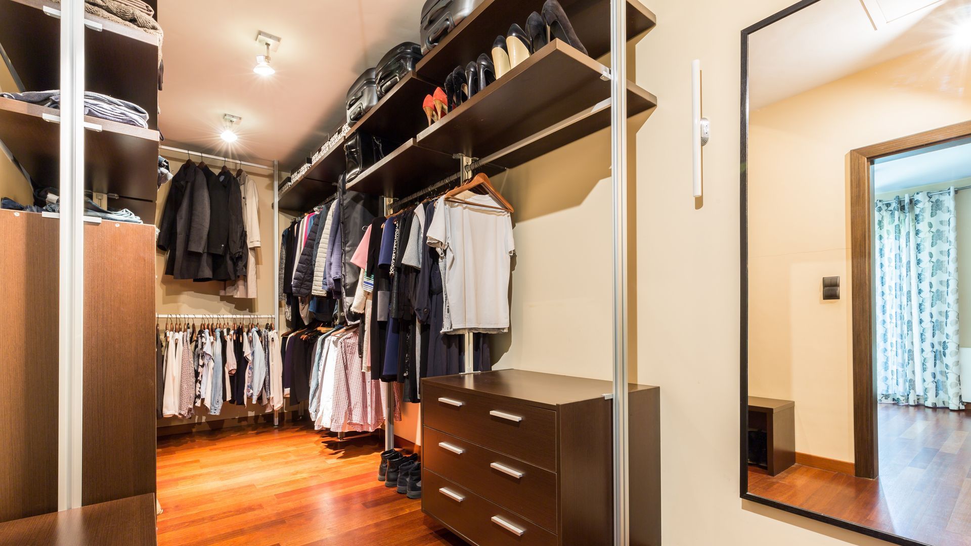 A walk in closet with lots of clothes and a mirror.