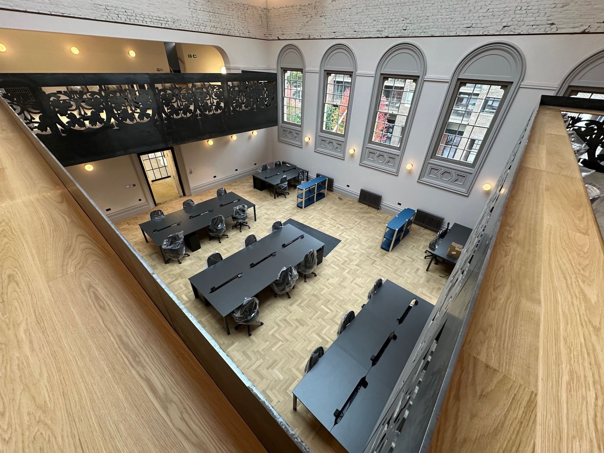 view from a ornate balcony looking down on to dark meeting tables, a parquet floor, large ornate arched stained glass windows.