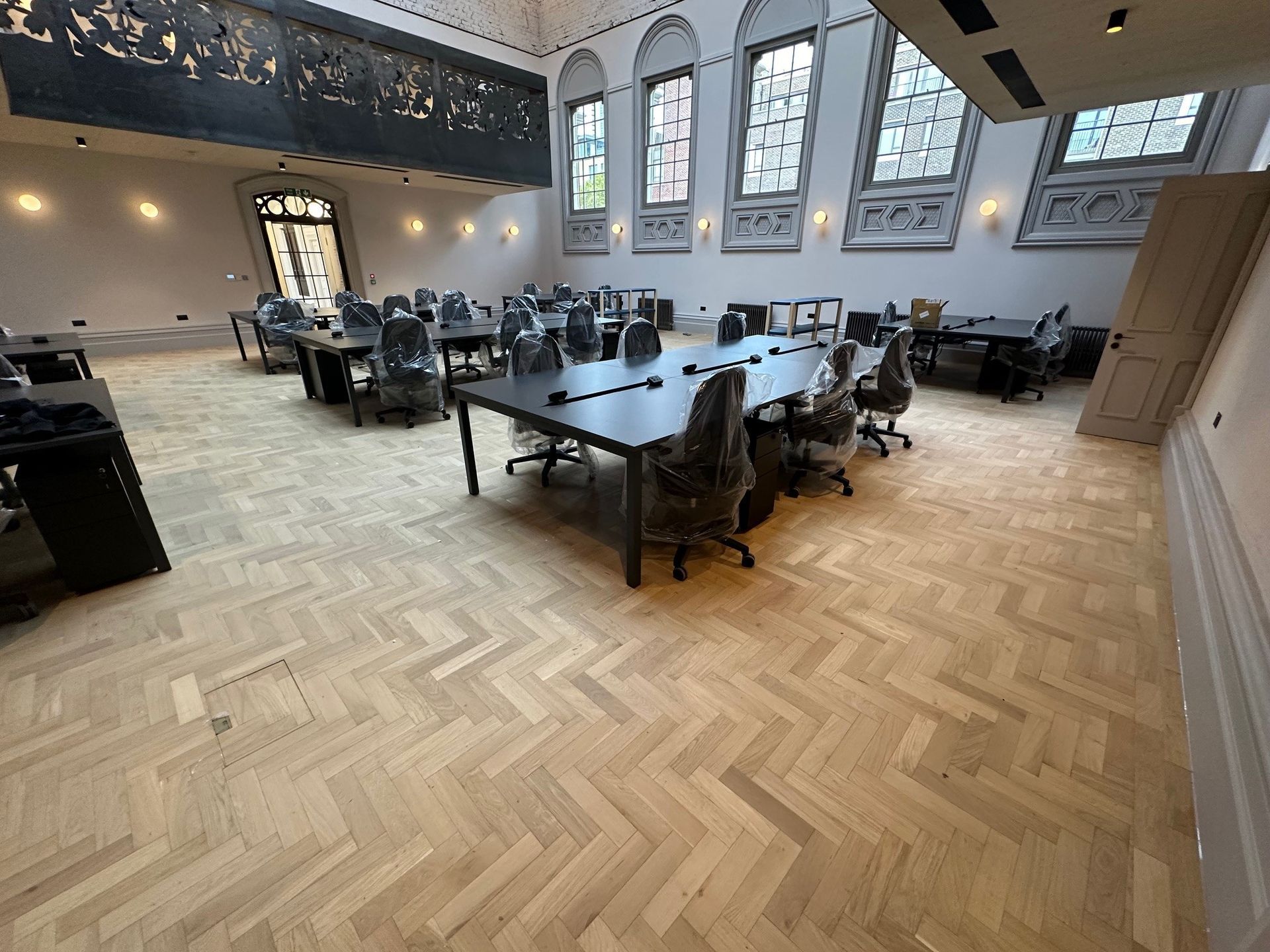 room with a parquet floor ornate stained glass arched windows and a black ornate balcony above 