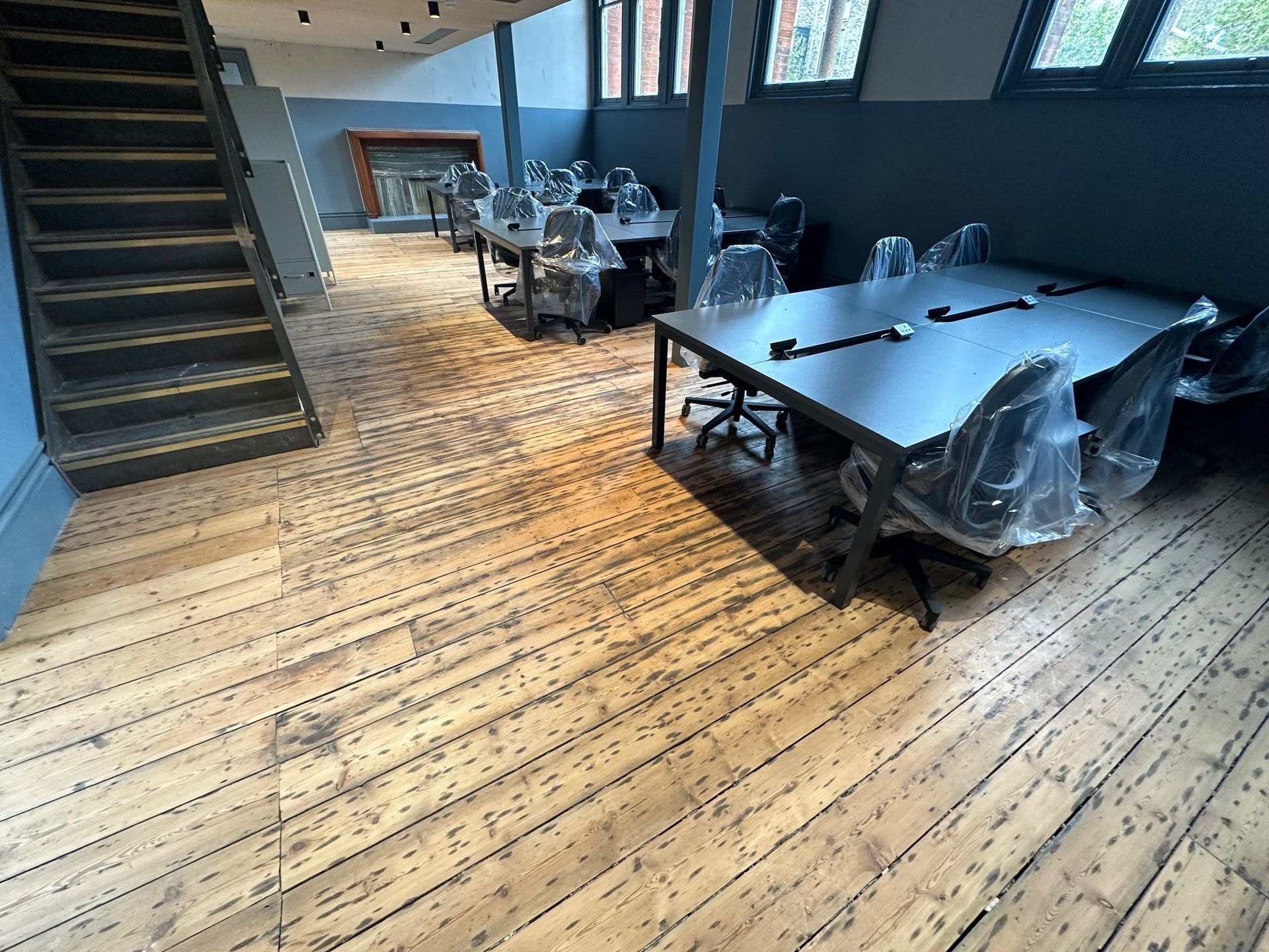 Aged wooden floor with a dark staircase , dark grey walls and dark meeting tables.