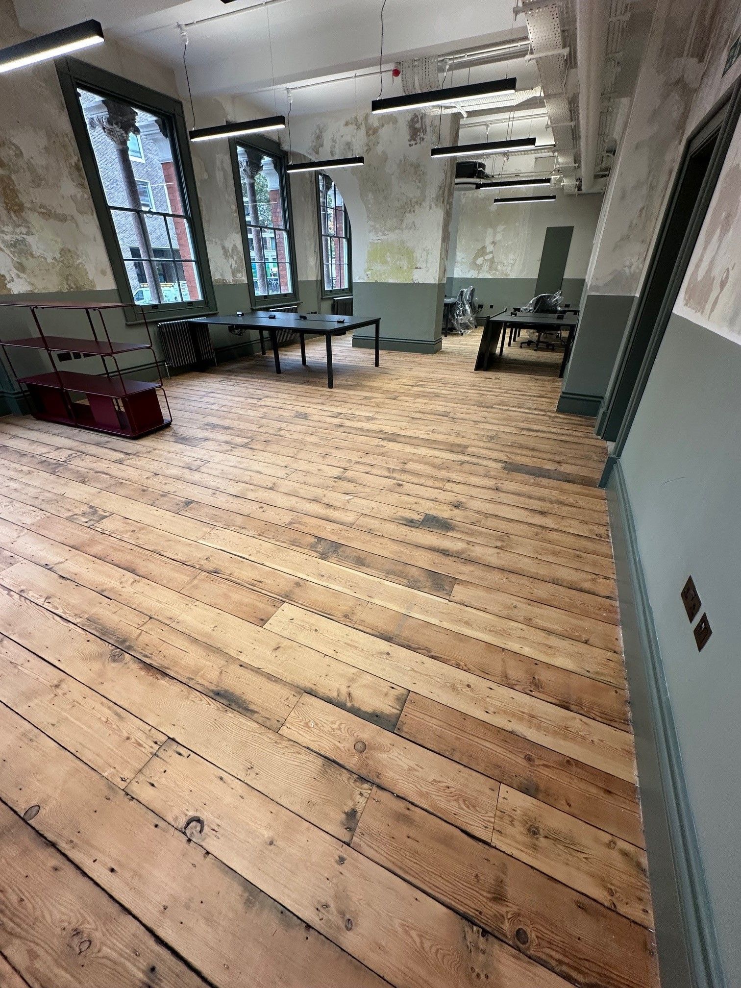 room with Aged wooden flooring with distressed painted walls and large arched windows with dark tables. 