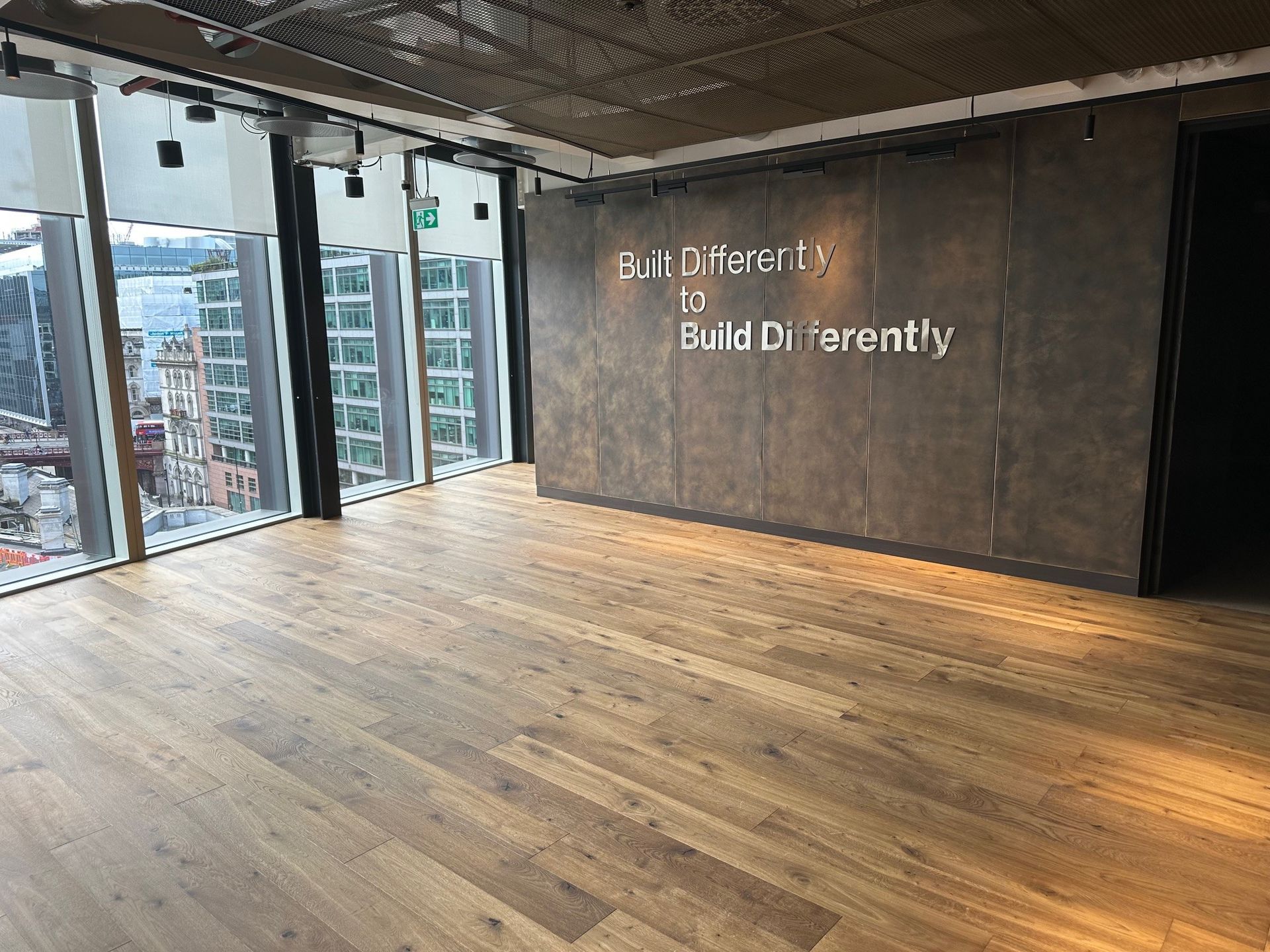 A large empty room with wooden floors and a wall that says `` build differently ''.