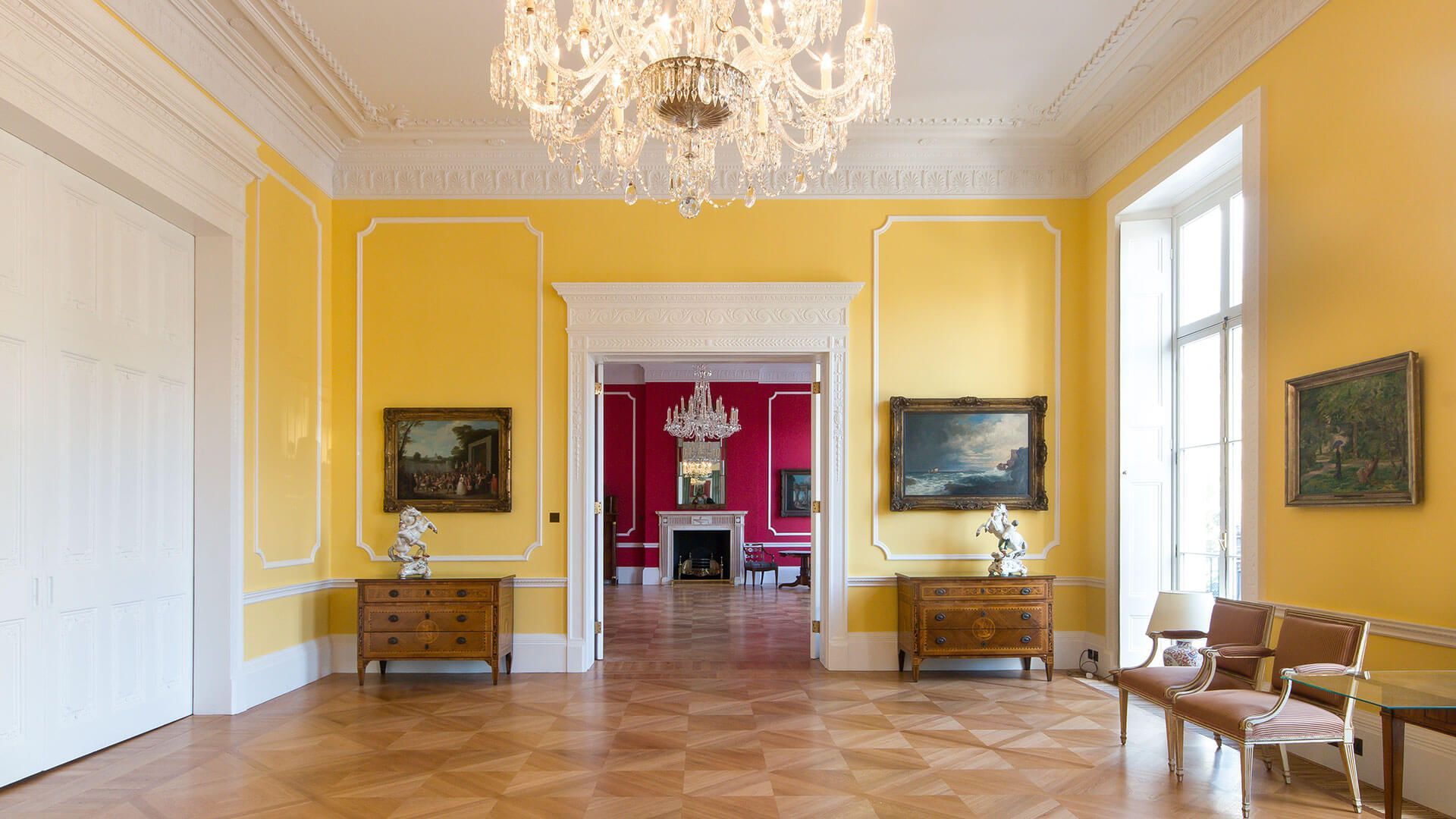 A large empty room with yellow walls and a chandelier hanging from the ceiling.