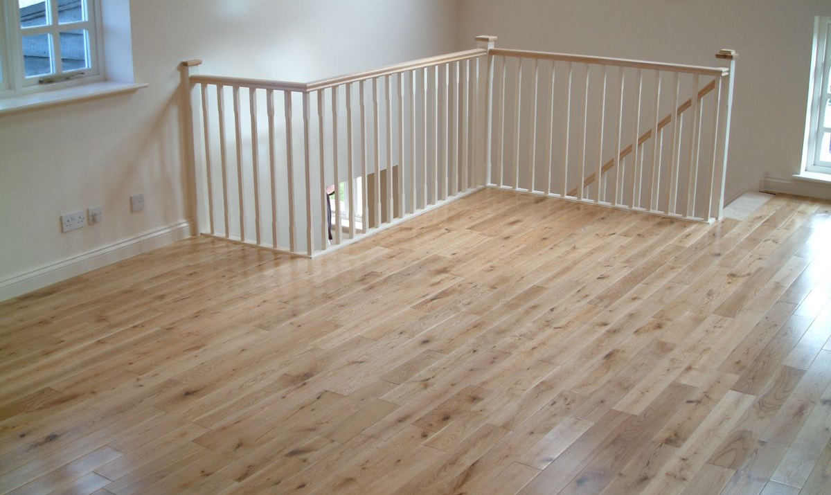 Light wood flooring and white railing enclose a stairway. Light wood flooring and white railing enclose a stairway. Sunlight streams in from windows.