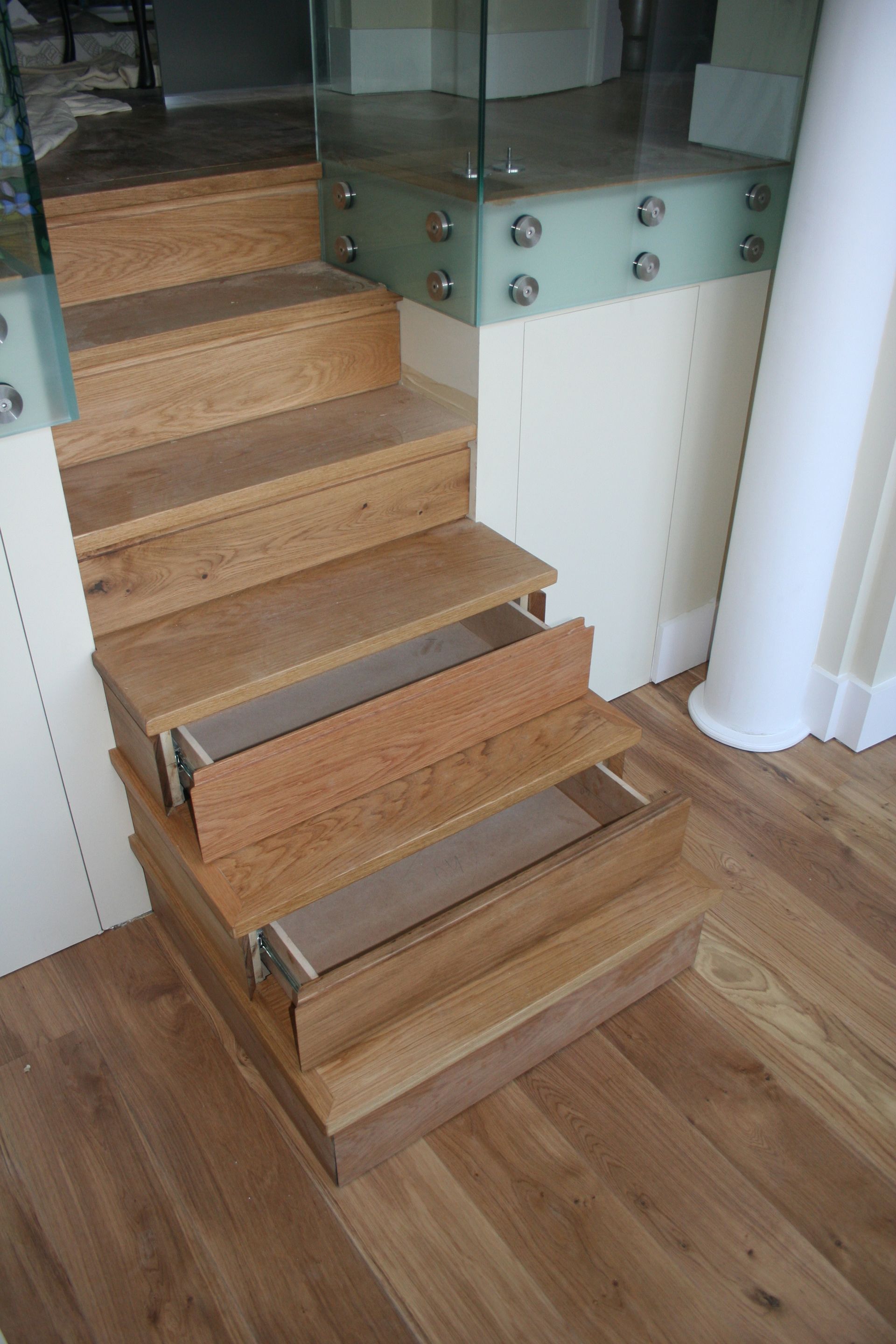 A wooden staircase with drawers underneath it and a glass railing.