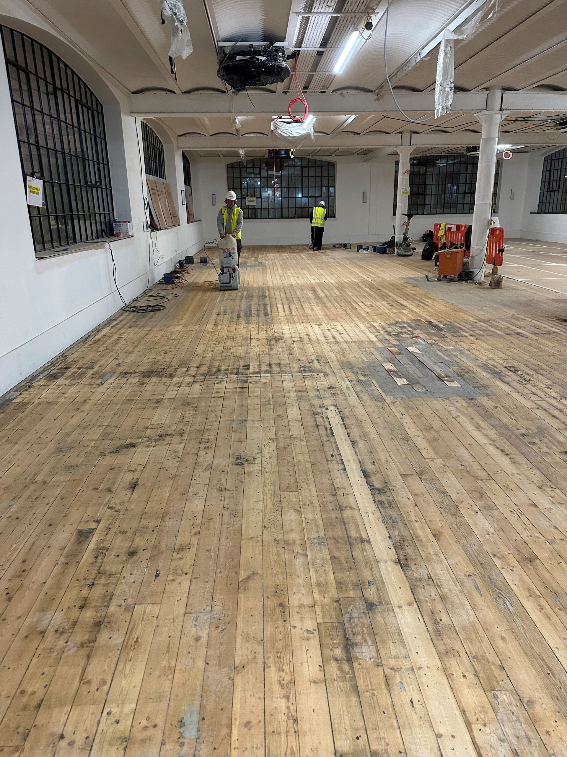 A large empty room with a wooden floor and a few people standing around.