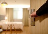 Person opening a hotel room door. Bedroom with bed and curtains in the background.