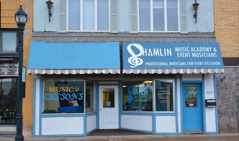The storefront of Hamlin Music Academy and Event Musicians with blue awnings and large display windows on a city street.