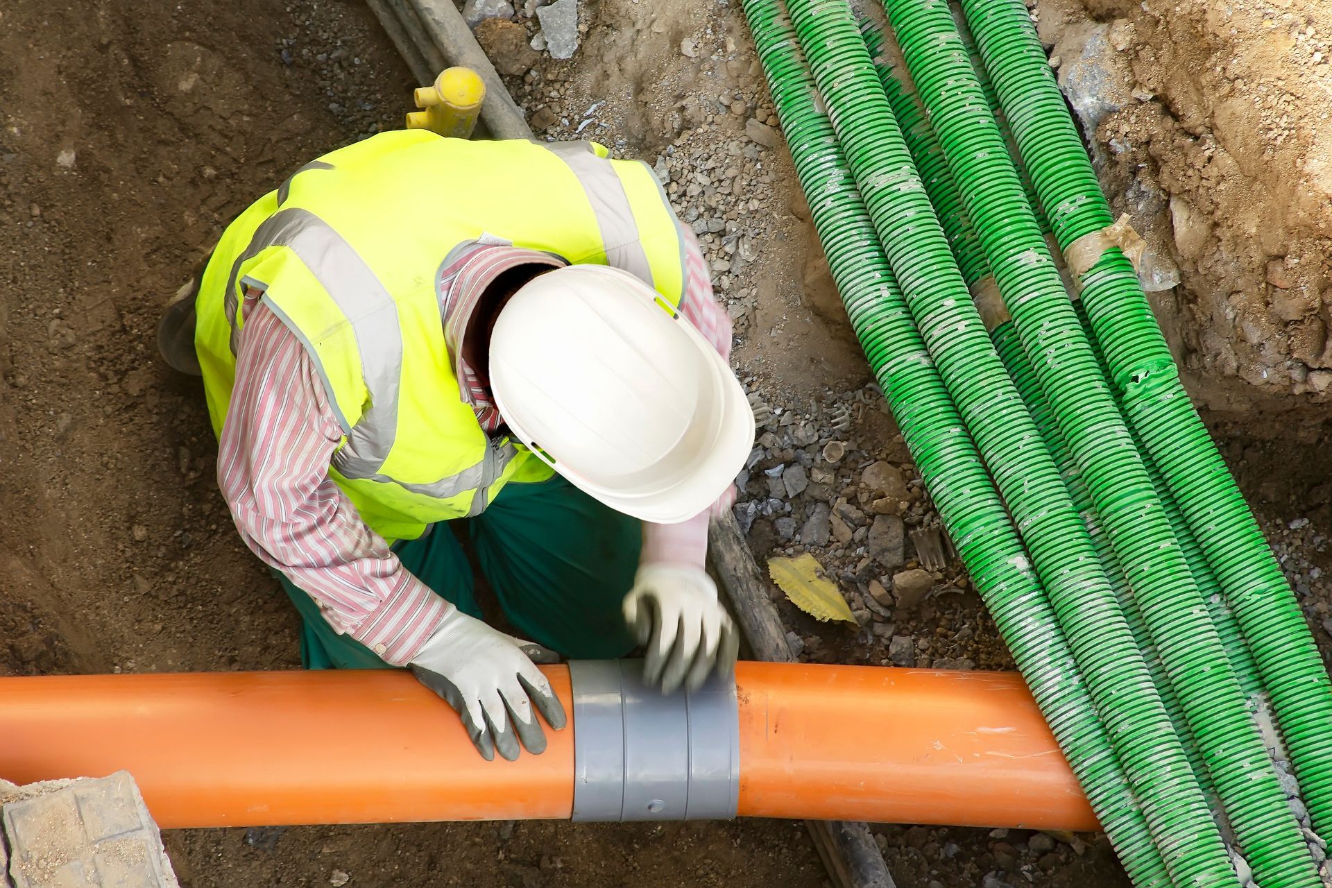 A construction worker is working on a pipe in the dirt.