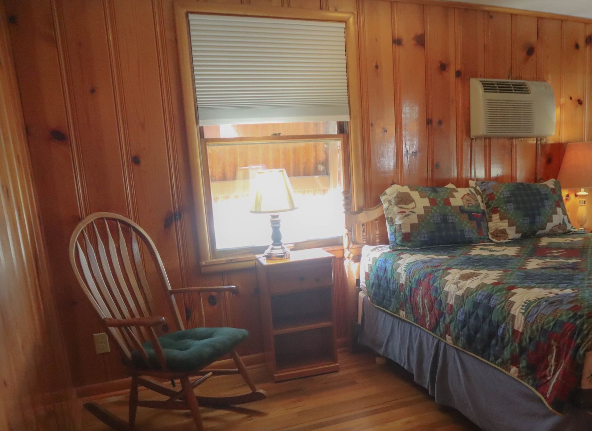 A bedroom with a bed , rocking chair , nightstand and window.