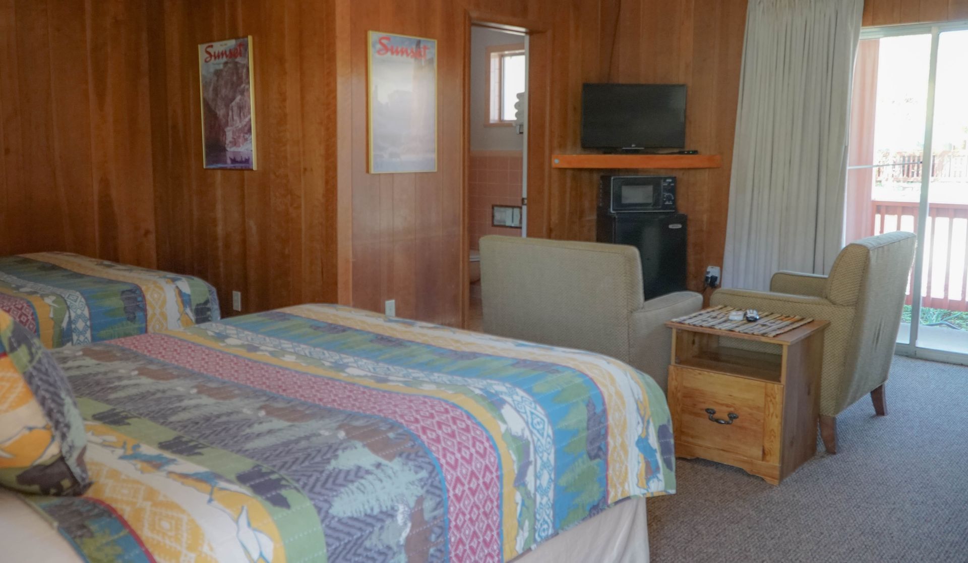 A hotel room with two beds , a chair , a television and a fireplace.