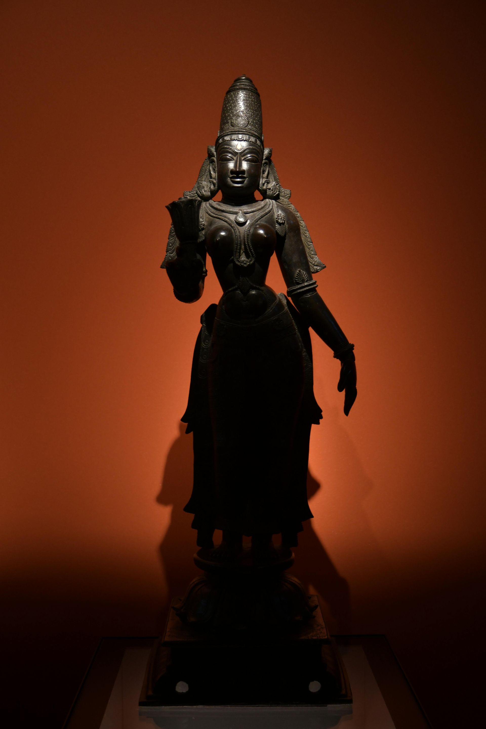 A statue of a woman standing in front of an orange wall.