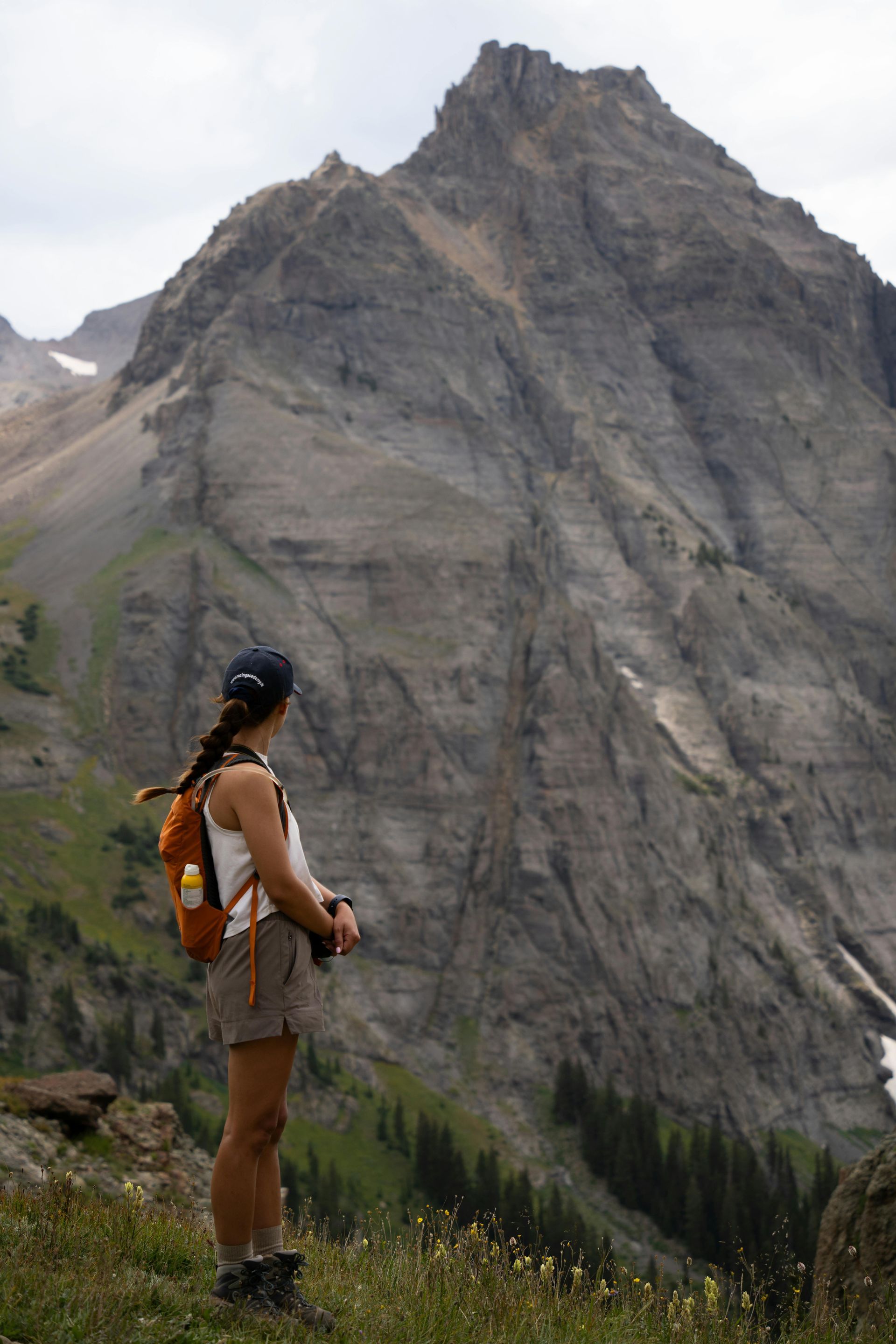 A woman with a backpack is standing in front of a mountain.