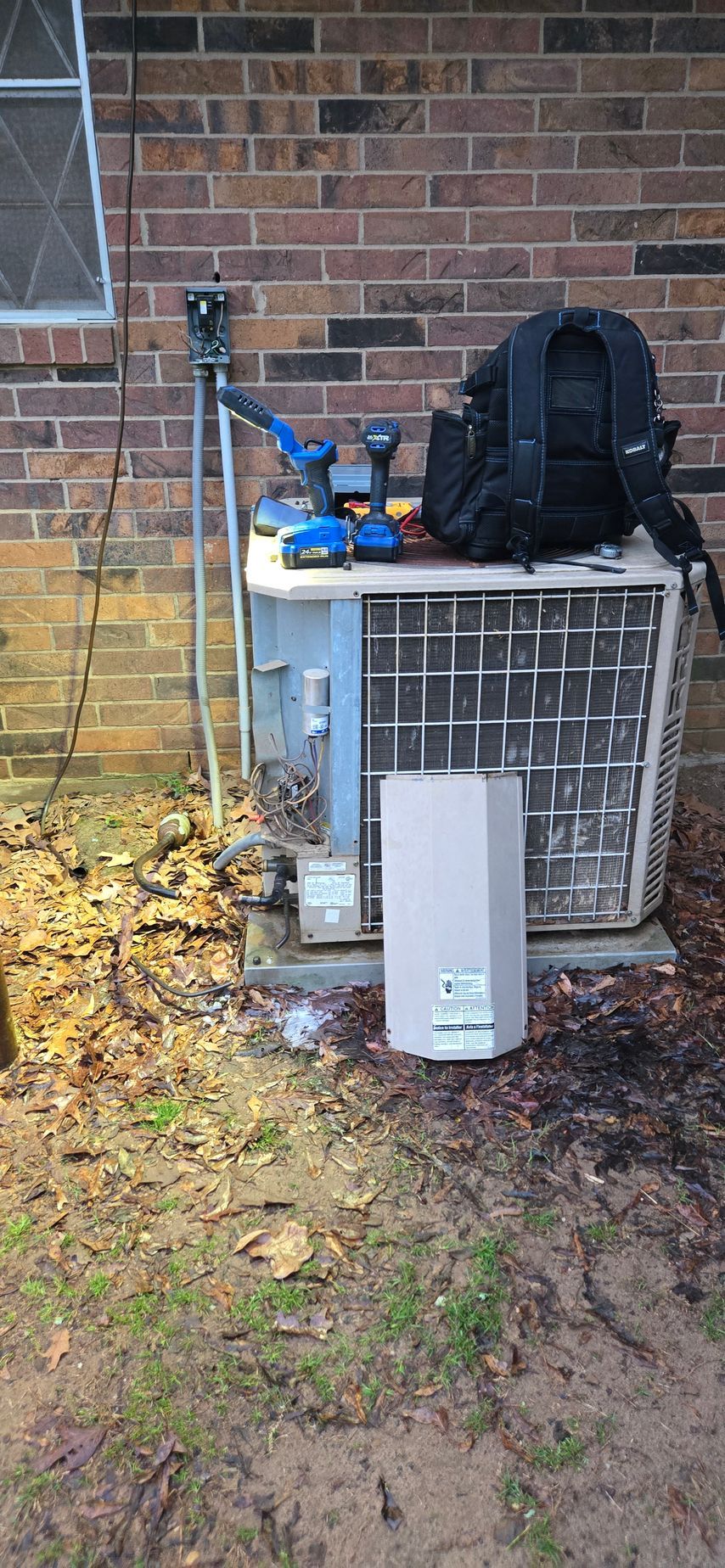An air conditioner is sitting on the side of a brick building.