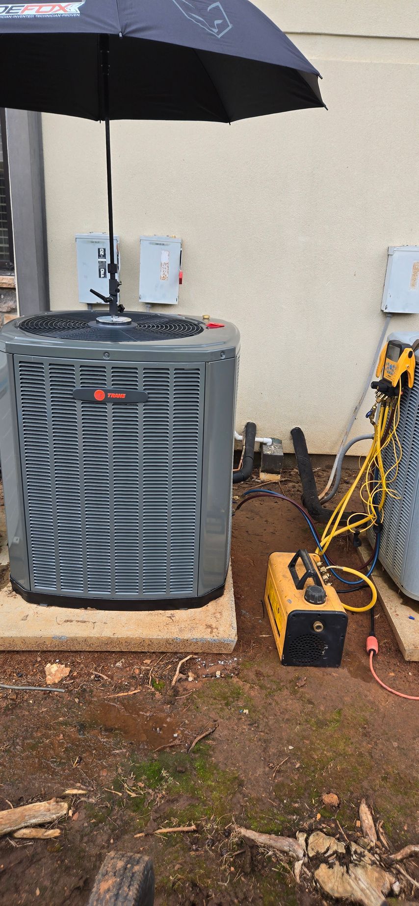 A large air conditioner is sitting under an umbrella on the side of a building.