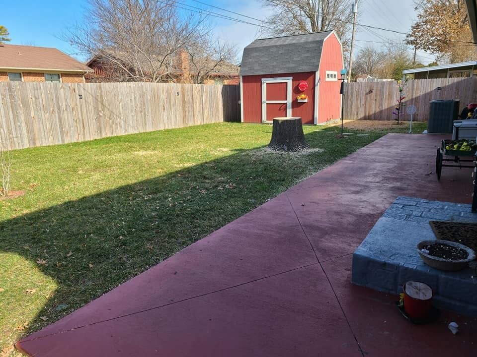 Backyard with red shed, wooden fence, green lawn, and a red concrete patio.