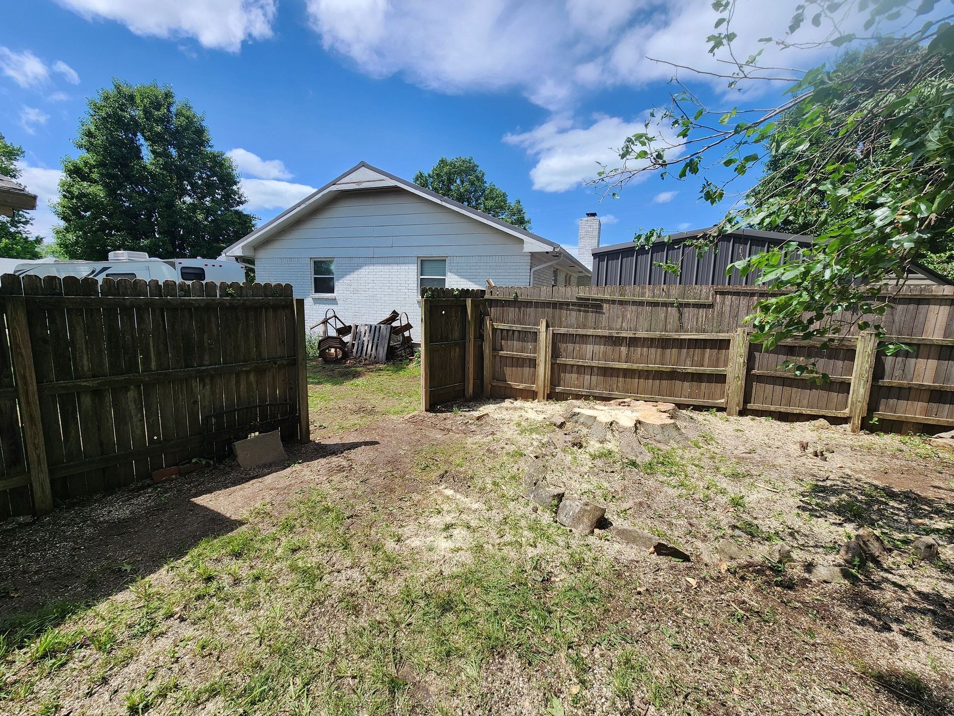 A backyard with a wooden fence and gate. A white house is in the background.