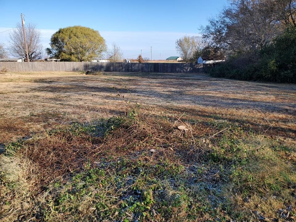 A vacant lot with brown grass and a wooden fence, under a partly cloudy sky.