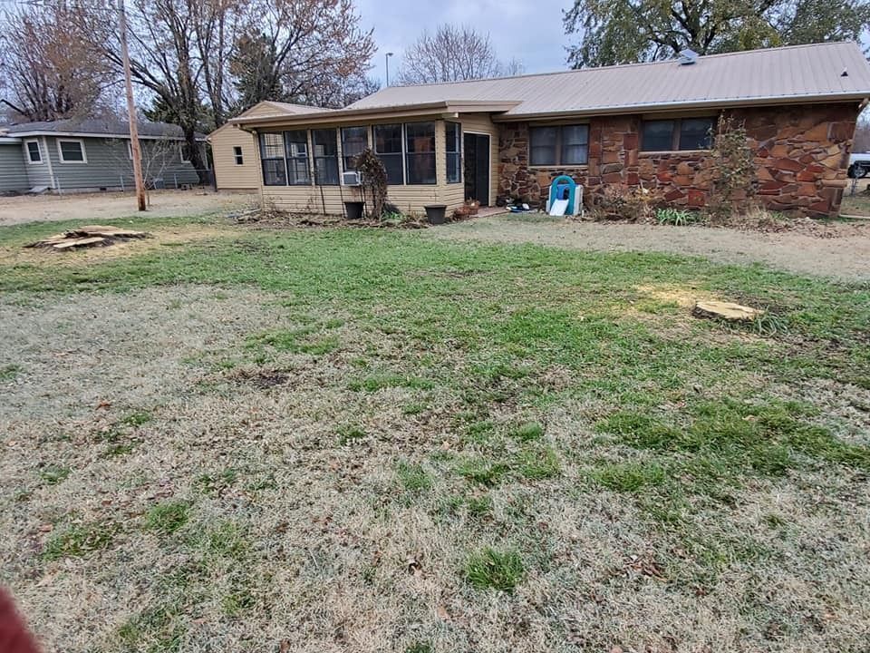 Ranch-style house with screened porch and brick exterior, set in a yard with grass and tree stumps.