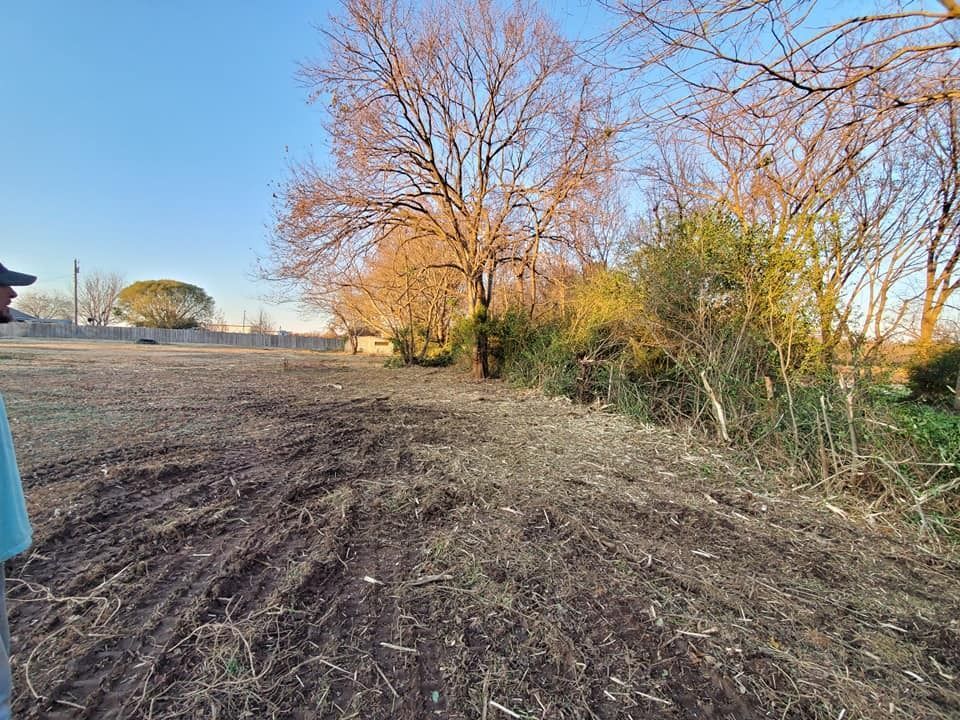 Person standing on a field. Bare trees and brush in the background with a blue sky.