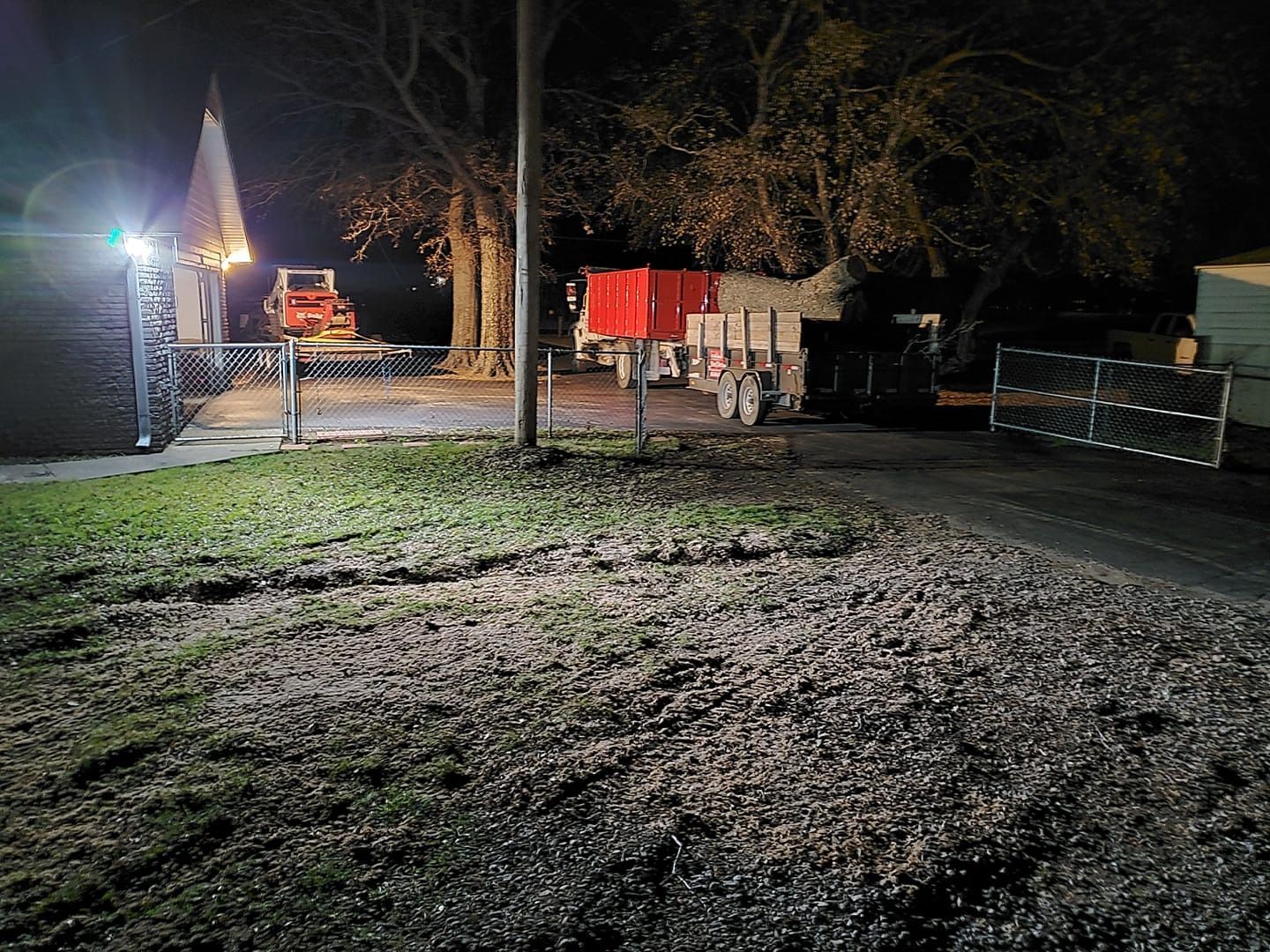 Nighttime scene: Gravel driveway, mailbox, parked truck, lit building. Bright spotlight on left.