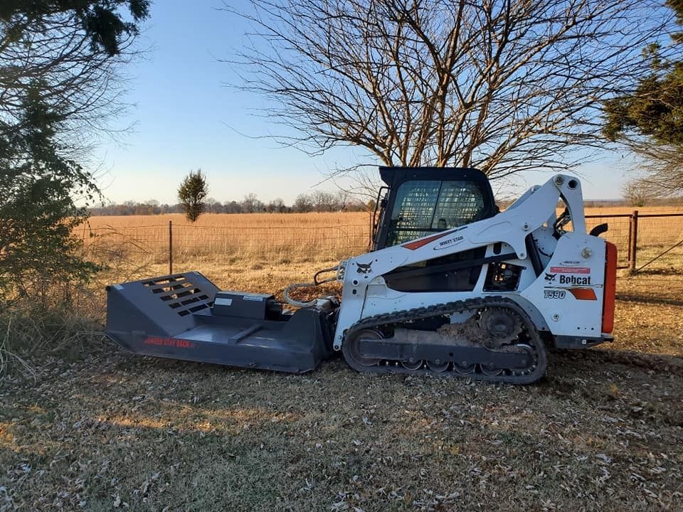 White Bobcat with a brush cutter attachment in a field.