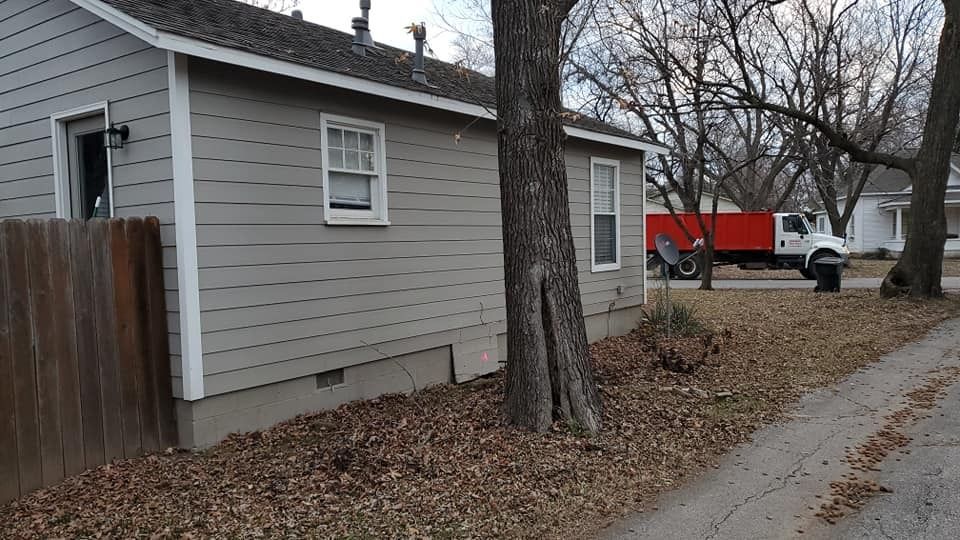 Side of a gray house with a brown fence and a large orange truck in the background on a street.
