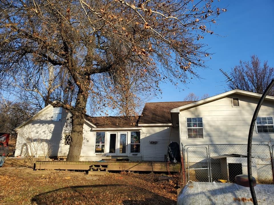 White house with brown roof, bare tree, wooden deck, clear blue sky.