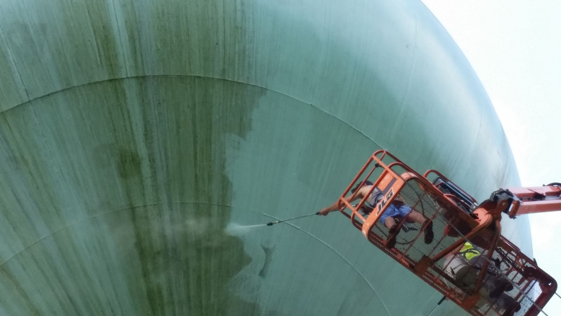 A crane is cleaning a large green tank with a hose.