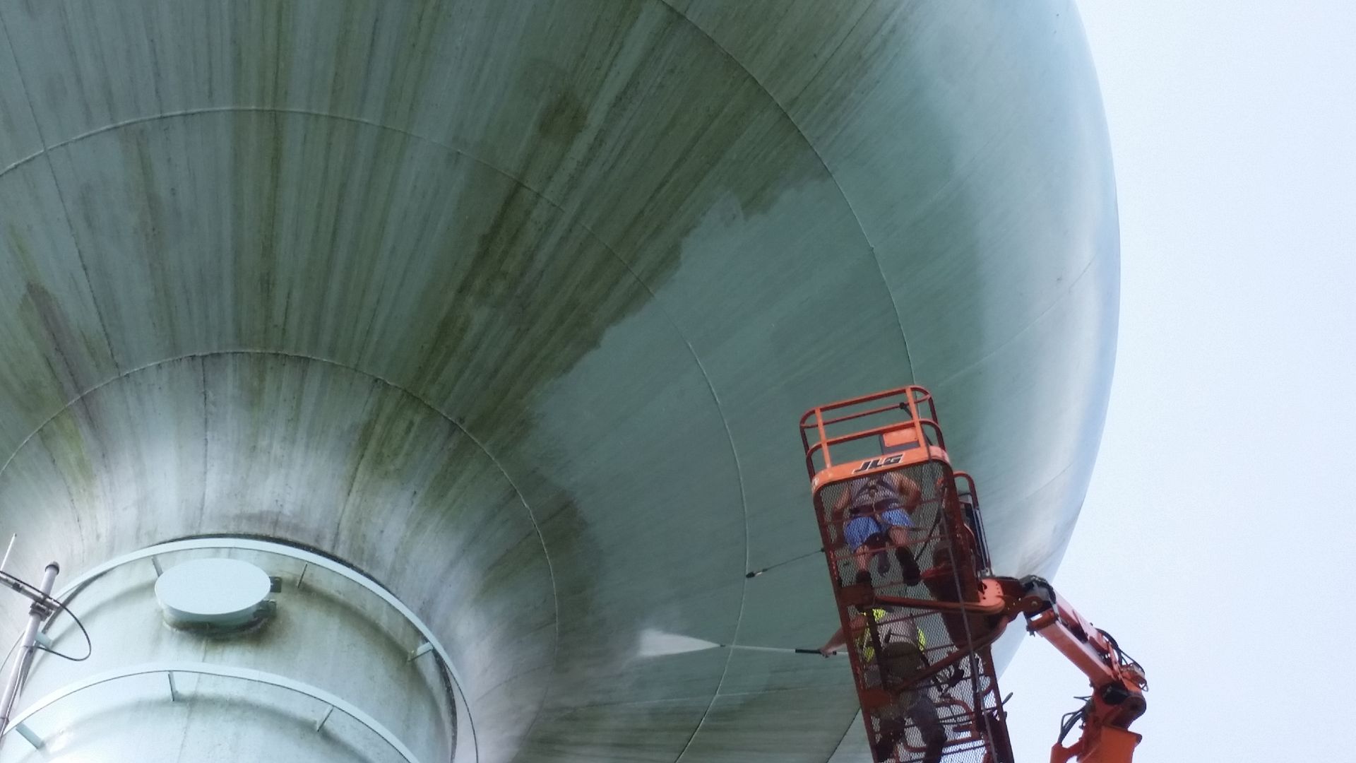A man is cleaning a large water tower with a crane.