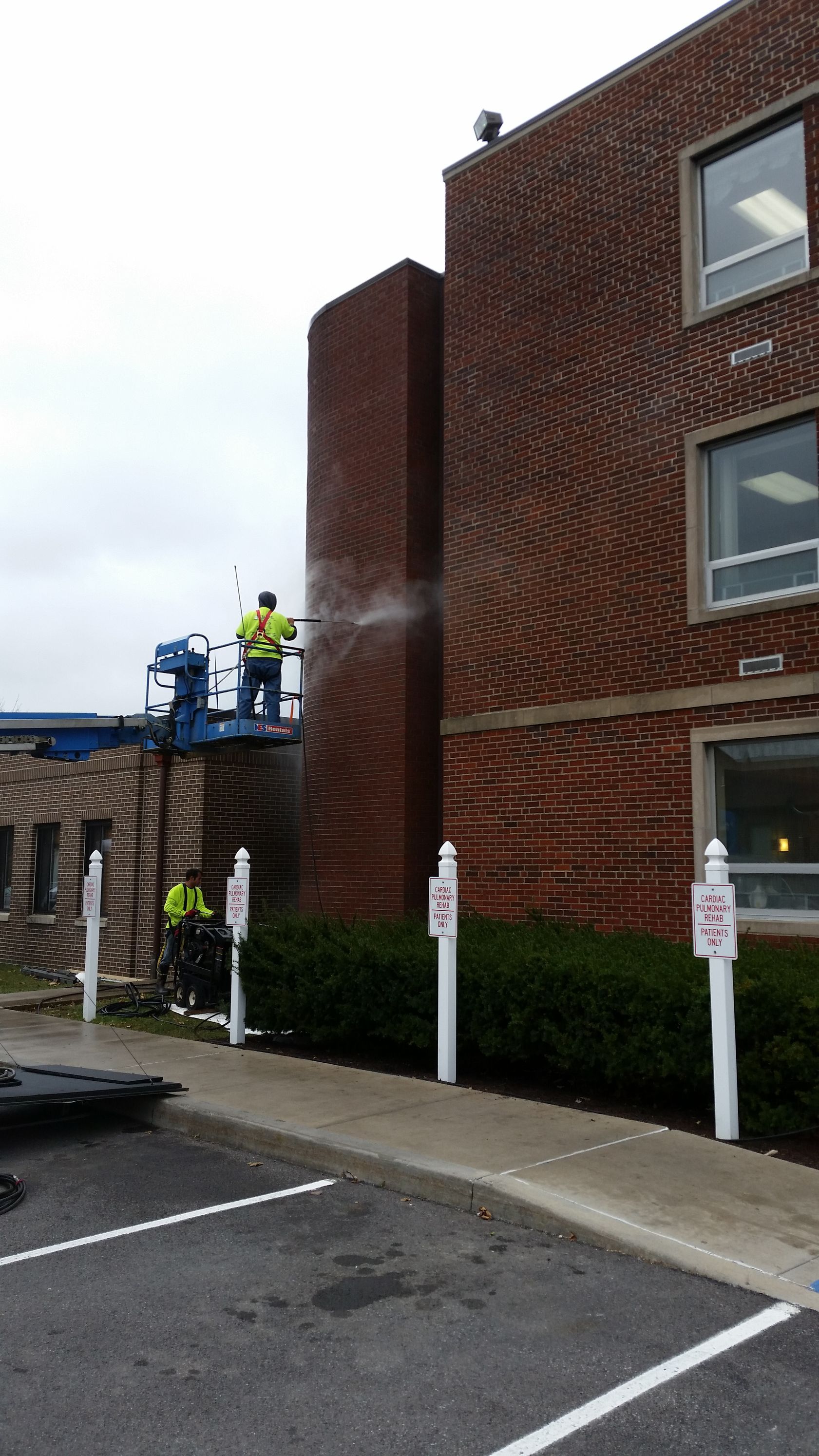 A man is cleaning a brick building with a high pressure washer.