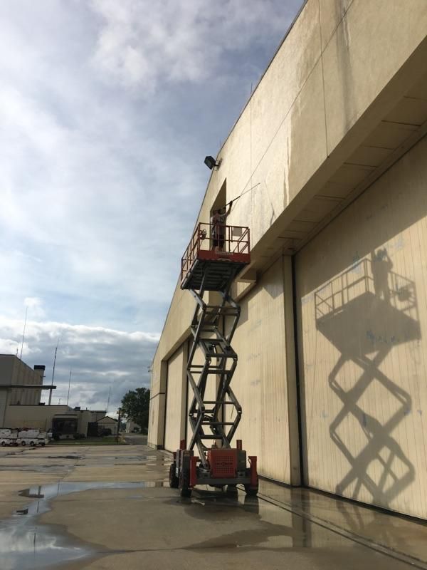 A man is standing on a scissor lift in front of a building.