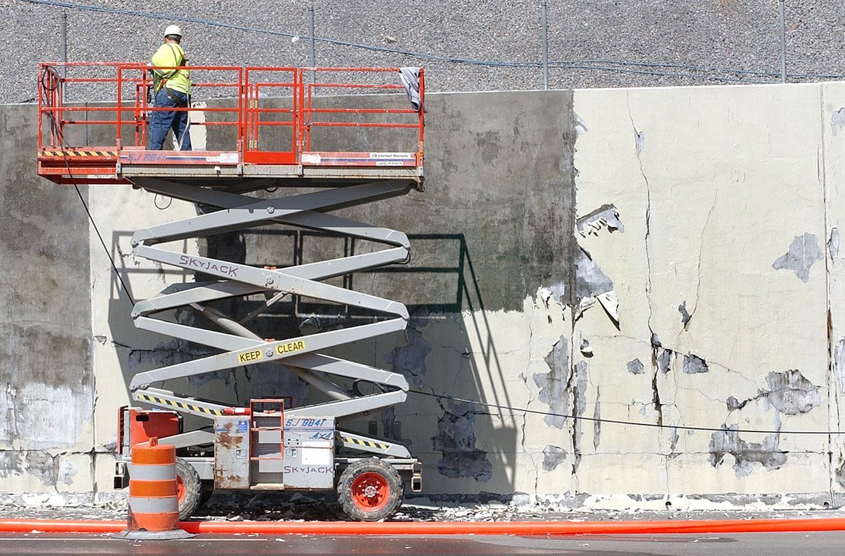 A man is standing on a scissor lift working on a wall.