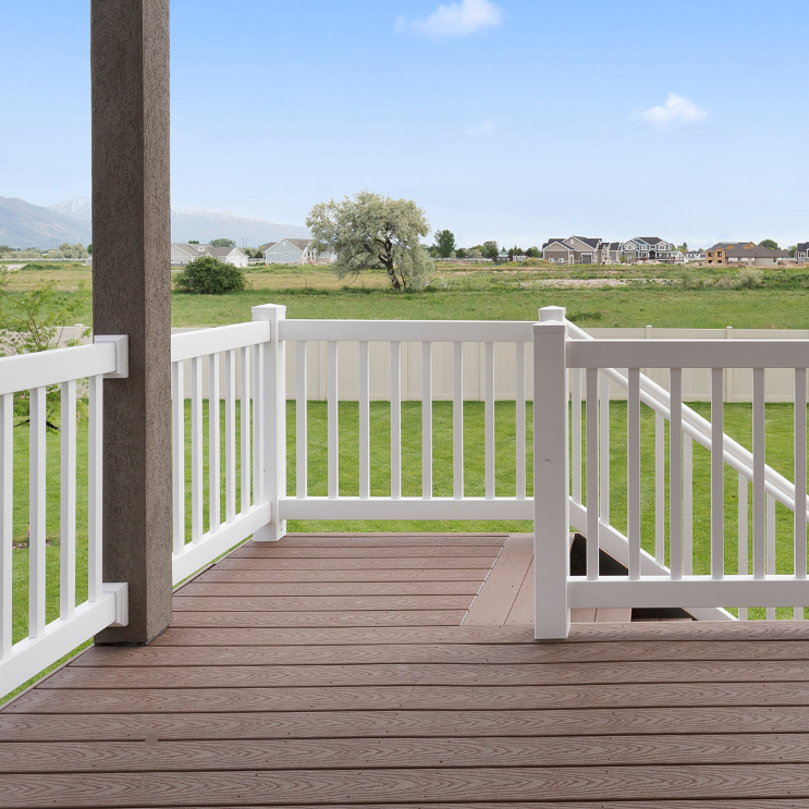 An empty deck with a white railing and a view of a field.