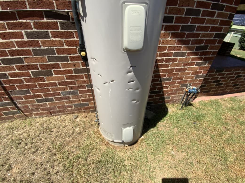 A White Water Heater Is Sitting In Front Of A Brick Wall — Able Building And Pest Inspections In Woolgoolga, NSW