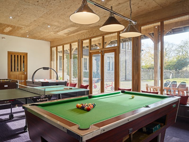 Bright game room with a pool table, air hockey table, wooden beams, and large windows.
