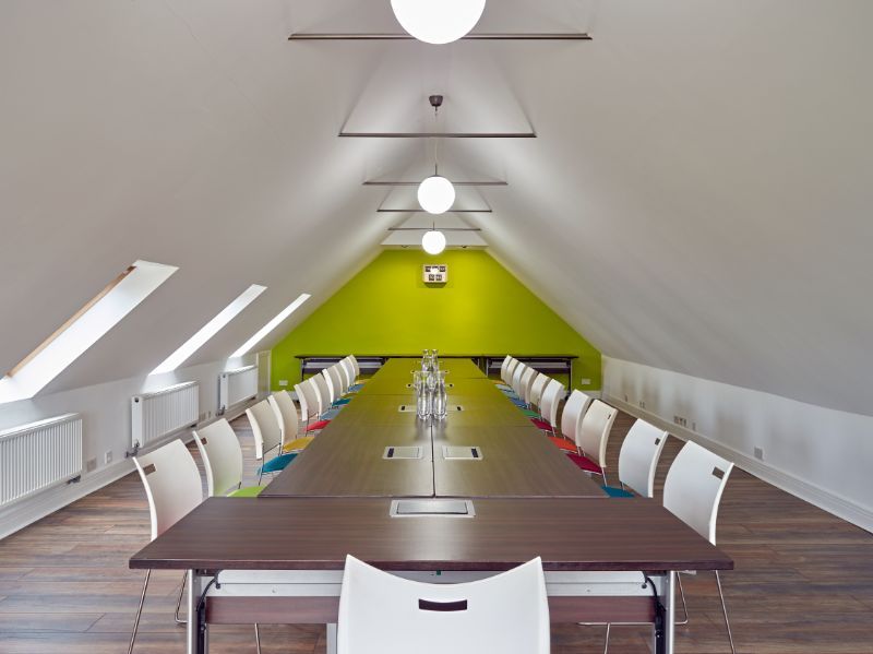 Long conference table in a bright attic meeting room with lime-green end wall and white chairs on both sides
